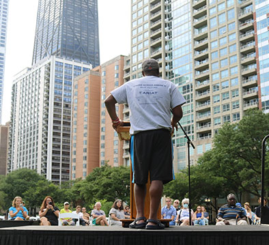 Back of a man giving a speech in a park in front of a large crowd
